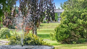 A well-maintained garden with a fountain, neatly trimmed hedges, and a building with a stone wall in the background. - 3 Bed in Uphill (oc-n27747) (Linkinhorne)
