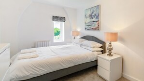 A bedroom with a bed, bedside lamps, a radiator, a window with a view, and a painting on the wall. - 2 Bed in Abersoch (oc-p27804) (Abersoch)
