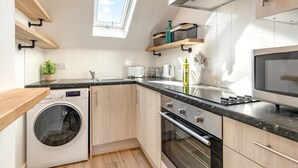 A modern kitchen with a washing machine, oven, and microwave. There is a window providing natural light and a view of the sky. - 2 Bed in Abersoch (oc-p27804) (Abersoch)