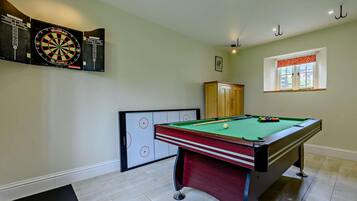A billiards room with a pool table, dartboards, and a cabinet.
