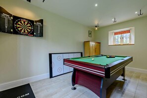 A billiards room with a pool table, dartboards, and a cabinet.