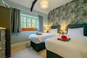 A hotel room with two beds, a dresser, a window with curtains, and a floral wallpaper.