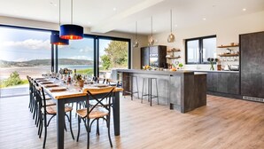 Une cuisine moderne dotée d’un grand îlot central, de tabourets de bar et d’un coin repas offrant une vue sur la mer.