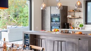 Une cuisine moderne dotée d’un îlot central, d’appareils électroménagers en acier inoxydable et de luminaires suspendus.