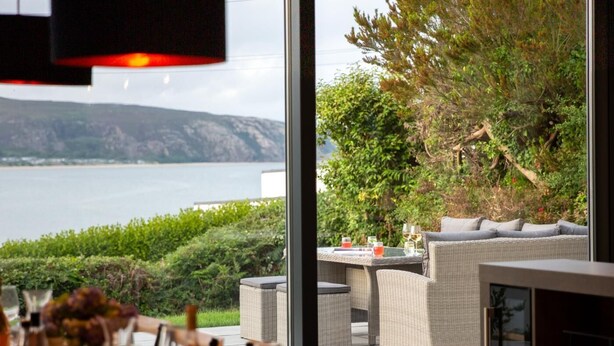 Un espace repas avec vue sur un lac et des montagnes. Il y a un coin salon extérieur avec une table et des chaises.