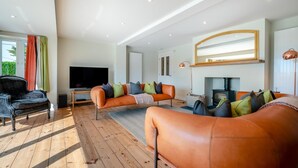 A spacious living room with a large orange sofa, a black armchair, and a television. - 6 Bed in Constantine Bay (oc-l27699) (Constantine Bay)