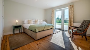 A bedroom with a bed, a nightstand, a chair, and a view through a sliding glass door. - 6 Bed in Constantine Bay (oc-l27699) (Constantine Bay)