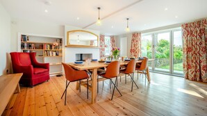 A modern dining area with a wooden table, red and orange chairs, and a bookshelf. - 6 Bed in Constantine Bay (oc-l27699) (Constantine Bay)