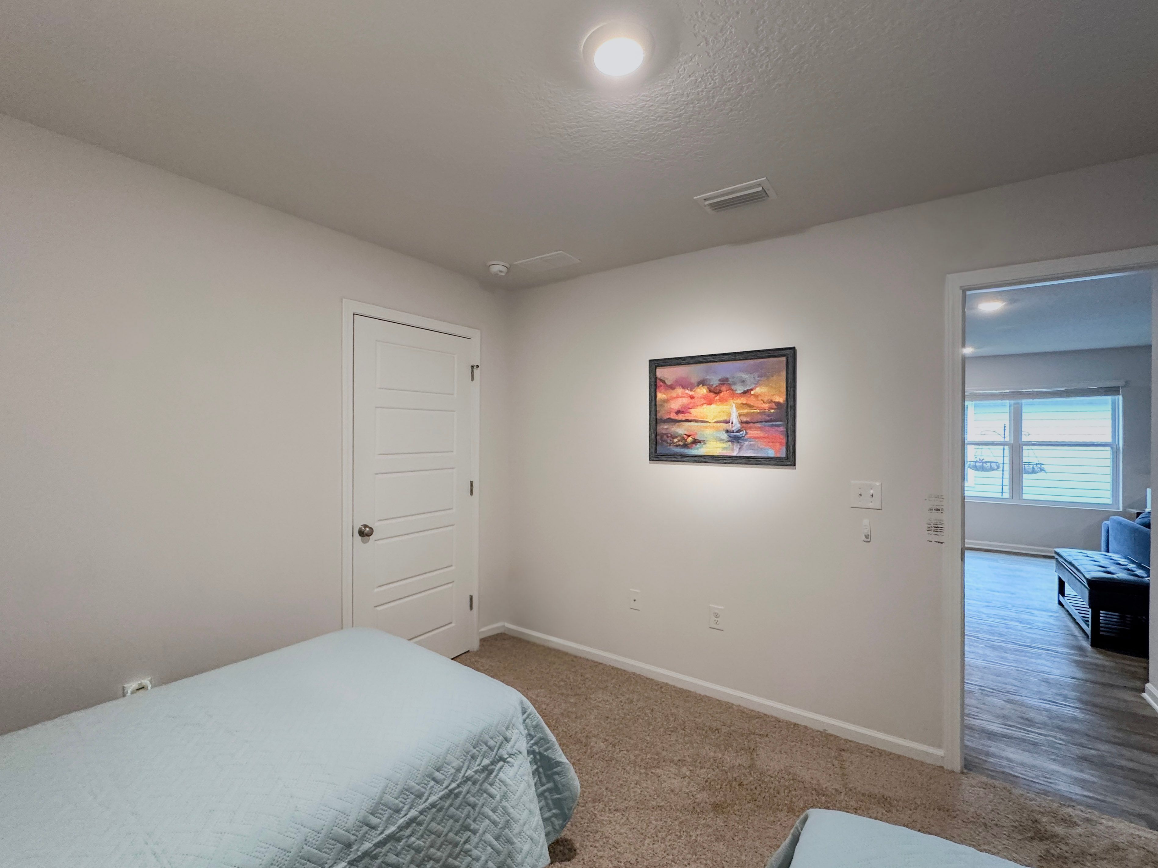 A bedroom with two beds, a door, a painting, and a hallway leading to another room.