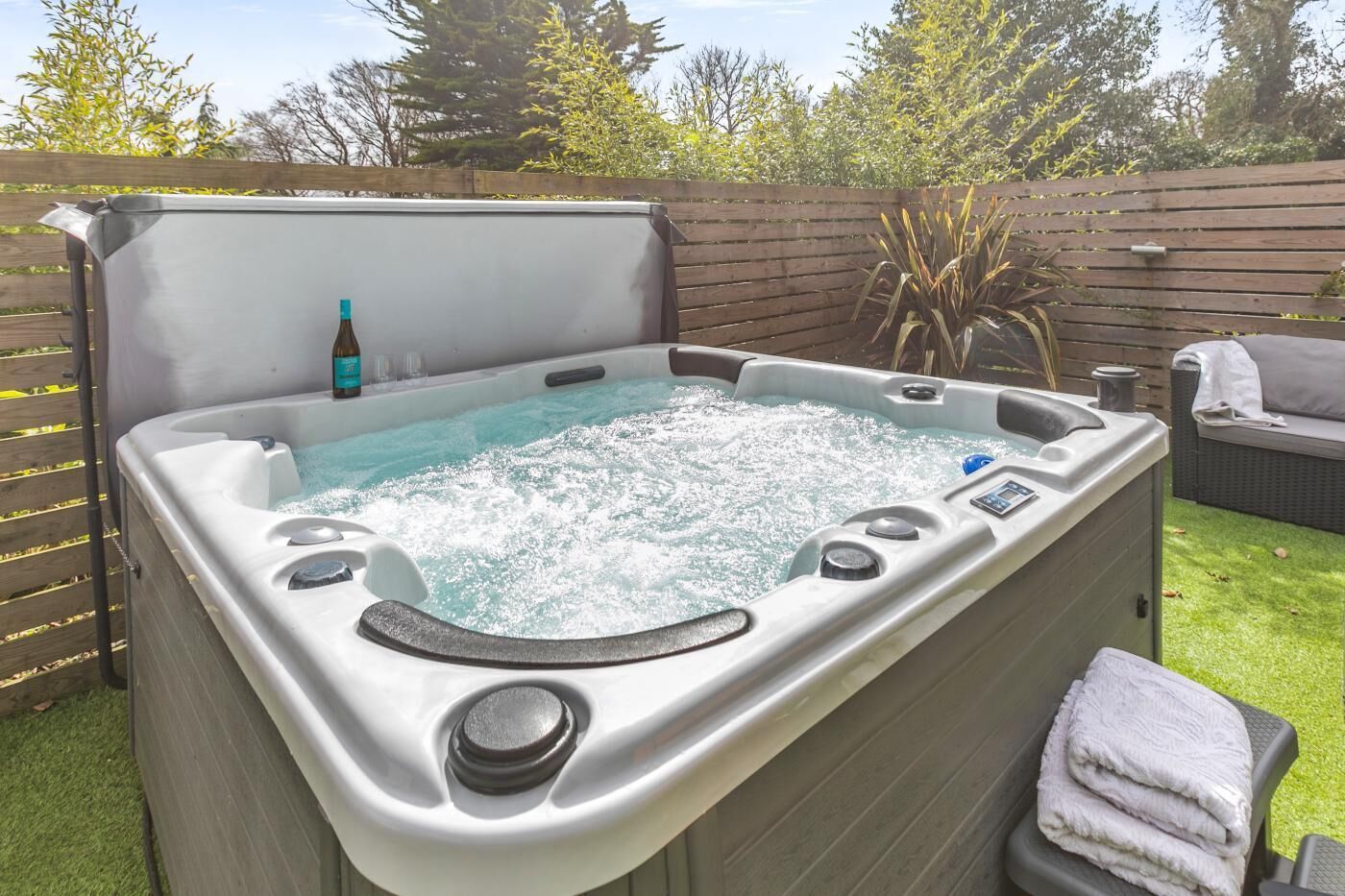 A hot tub with a control panel, a bottle, and a towel on a patio.