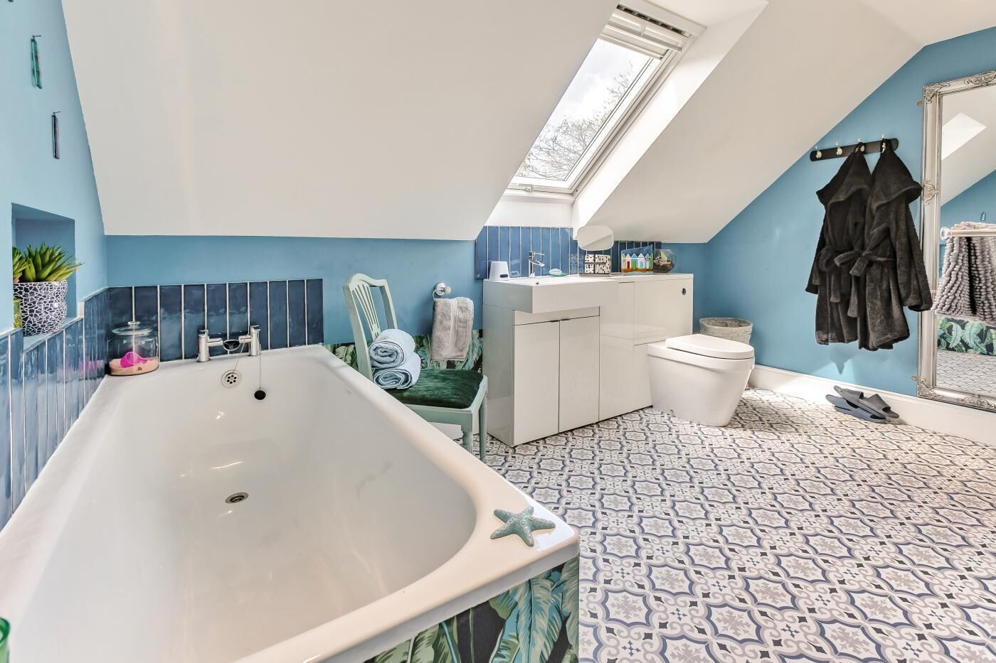 Un baño moderno con bañera, inodoro y lavabo, con paredes azules y baldosas de suelo estampadas.