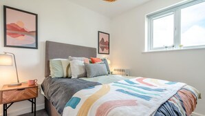 Ein Schlafzimmer mit einem Bett, einem Nachttisch, einer Lampe und zwei gerahmten Bildern an der Wand.