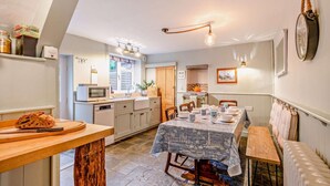 A cozy kitchen with a dining area, featuring a wooden table, a built-in oven, and a hanging light fixture. - 3 Bed in Wells-next-the-Sea (oc-c27939) (Wells-next-the-Sea)