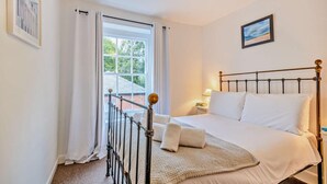 A bedroom with a bed, a nightstand, a lamp, a window with curtains, and a picture on the wall. - 3 Bed in Wells-next-the-Sea (oc-c27939) (Wells-next-the-Sea)