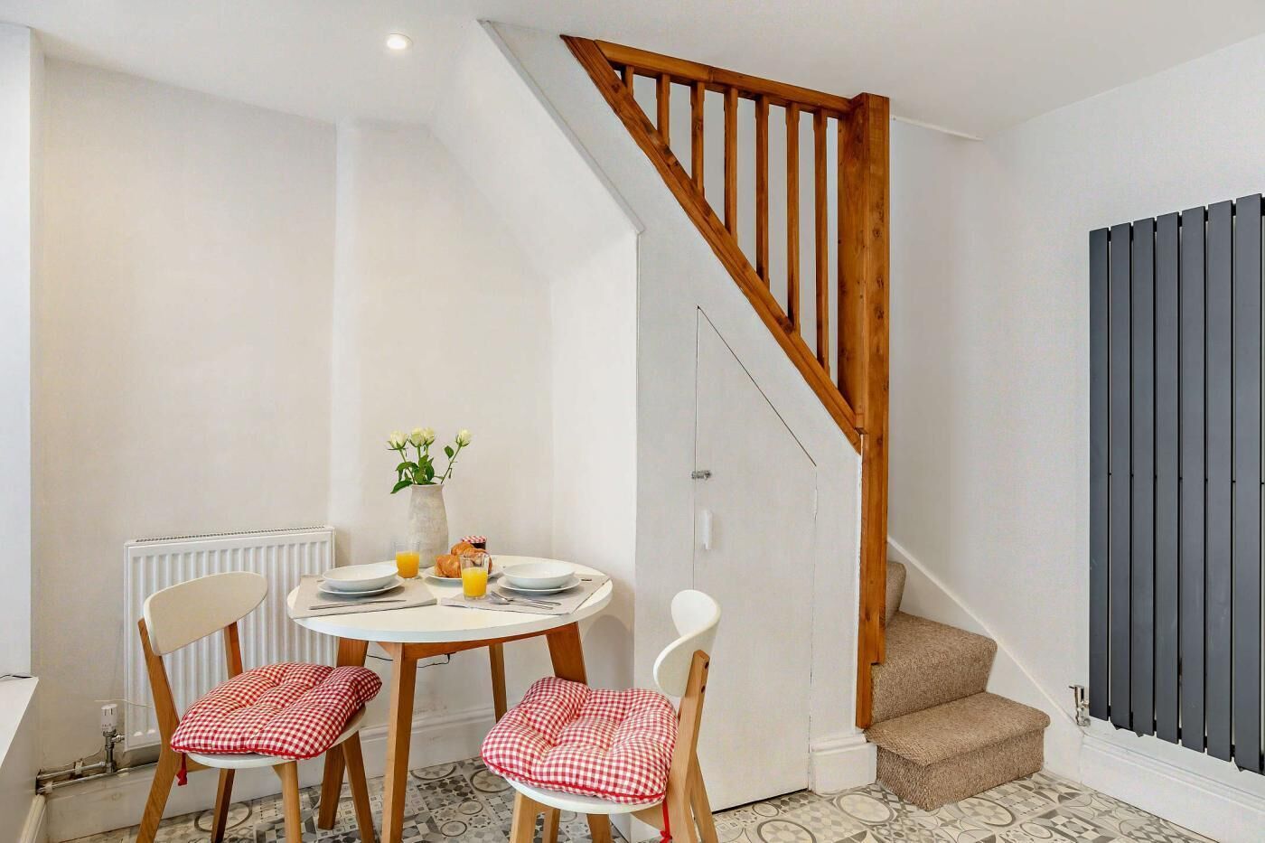 A dining area with a round table, two chairs, a vase with flowers, and a breakfast setting.