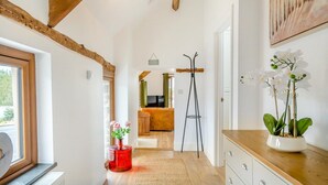 Un couloir avec des poutres en bois, un vase rouge rempli de fleurs, un lampadaire et un tableau accroché au mur.