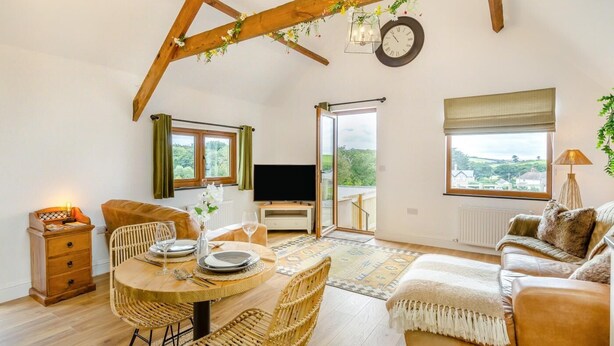 Un salon chaleureux avec un plafond en bois, une table à manger dressée pour quatre personnes, un canapé et un téléviseur.