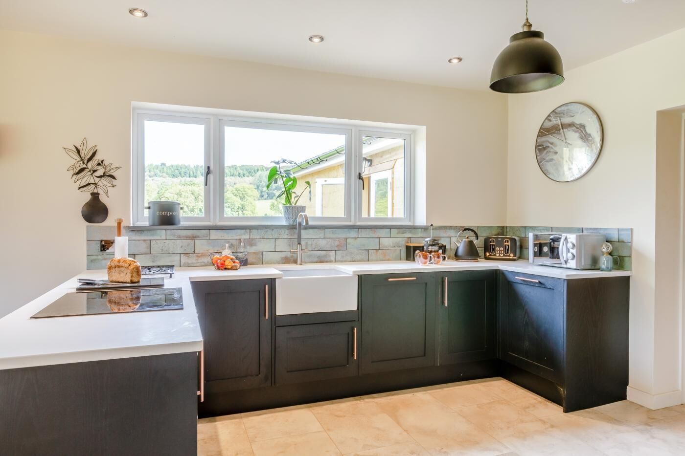 Een moderne keuken met donkere kastjes, een groot raam en een hangende pendellamp.