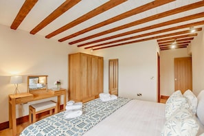 A bedroom with a wooden ceiling, a bed with patterned bedding, a wooden wardrobe, a bedside table with a lamp, and a bench. - 5 Bed in Menai Bridge (oc-t23240) (Menai Bridge)
