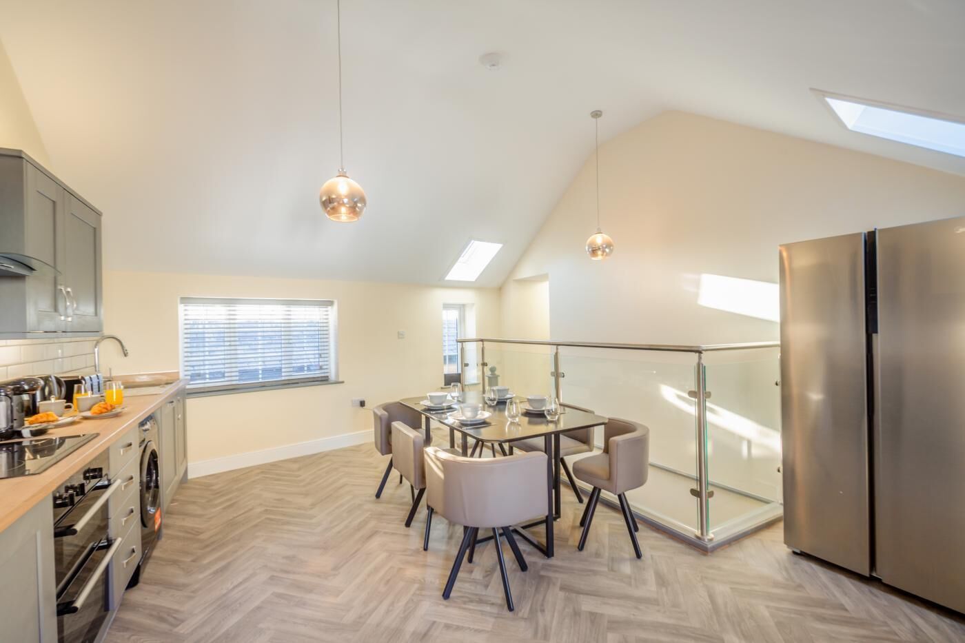 A modern kitchen with a dining area, a large refrigerator, and a skylight.