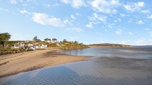 A coastal area with a sandy beach, calm water, and houses in the background. - 2 Bed in Abersoch (oc-r26047) (Abersoch)