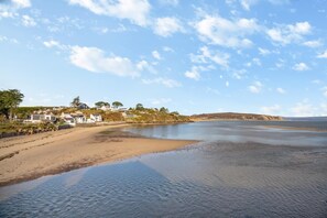 A coastal area with a sandy beach, calm water, and houses in the background. - 2 Bed in Abersoch (oc-r26047) (Abersoch)
