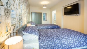 A bedroom with two beds, a large wall mural, a TV, and a window. - 2 Bed in Abersoch (oc-r26047) (Abersoch)