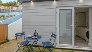 En terrasse med et bord og stole, kaffeudstyr og en skydedør, der fører til et køkken.