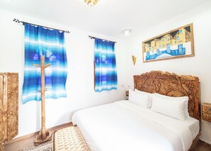 A bedroom with a bed, curtains, a wooden headboard, a painting, and a wooden coat rack. - PALACIO DEL SOL (Chefchaouen)