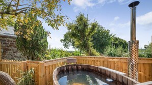 Un bain à remous en bois, doté d’un réchauffeur en métal, entouré d’une terrasse en bois et d’un mur en pierre.