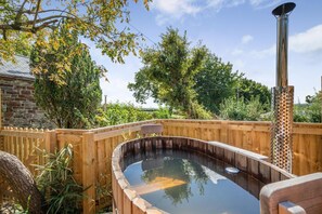 Ein hölzernes Whirlpool mit einem Metallbrenner, umgeben von einer Holzterrasse und einer Steinmauer.