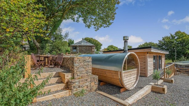 Une cabane rustique avec une cheminée en pierre, une structure en forme de tonneau en bois et un petit bâtiment attenant.