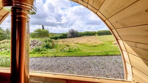 Une structure en bois offrant une vue sur un champ verdoyant et un ciel nuageux.