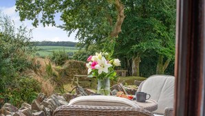 Un ensemble de meubles de jardin en osier, comprenant une chaise et une table, agrémenté d’un vase de fleurs, d’une tasse et d’une assiette de nourriture.