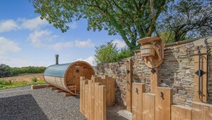 Un sauna doté d’un mur en pierre et d’une clôture en bois, intégré dans un paysage naturel.