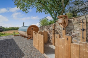 Eine Sauna mit Steinwand und Holzlattenzaun, eingebettet in eine natürliche Landschaft.