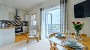 A modern kitchen with a dining area, a flat-screen TV, and a balcony with a view. - 2 Bed in Penally Near Tenby (oc-g28130) (Penally)