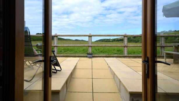 A view from a balcony with a metal railing, a paved floor, and a grassy field in the background. - 1 Bed in Morwenstow (oc-r28167) (Woodford)