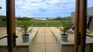 A patio with two potted plants, a wooden fence, and a view of the countryside. - 1 Bed in Morwenstow (oc-j28166) (Woodford)