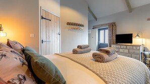 Un dormitorio con cama, televisor, cómoda y ventana con cortinas.