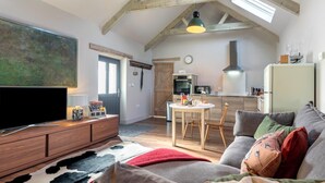 Una sala moderna con televisor de pantalla plana, muebles de madera, una mesa de comedor con sillas y una zona de cocina con estufa y microondas.