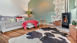 Una sala de estar acogedora con un sofá gris, una manta roja, un tapiz de cuero blanco y negro, un taburete de madera y una chimenea moderna.