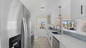 Cucina moderna con mobili bianchi, elettrodomestici in acciaio inossidabile e vista all'esterno.