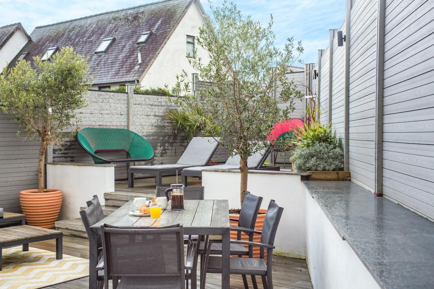 A patio area with a table and chairs, a green chair, and potted plants.