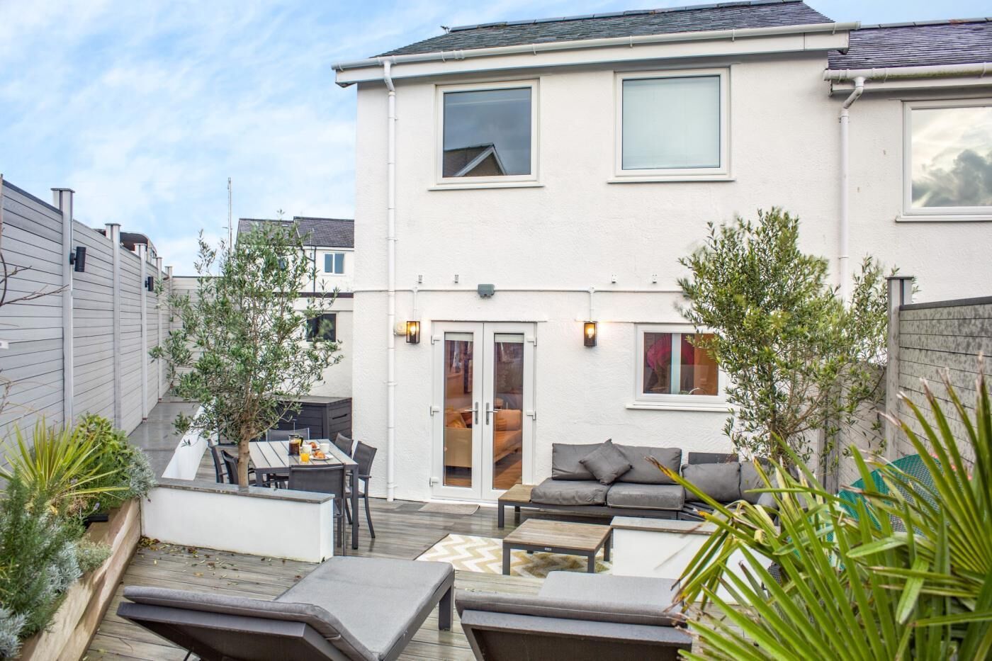 A two-story house with a patio area featuring a dining table, chairs, and a sofa.