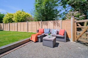 An outdoor seating area with a sofa and coffee table, a wooden gate, and a grassy lawn. - 1 Bed in Kilkhampton (oc-s28185) (Kilkhampton)