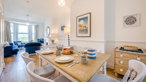 Un coin repas avec une table en bois dressée pour quatre personnes, entourée de chaises blanches.