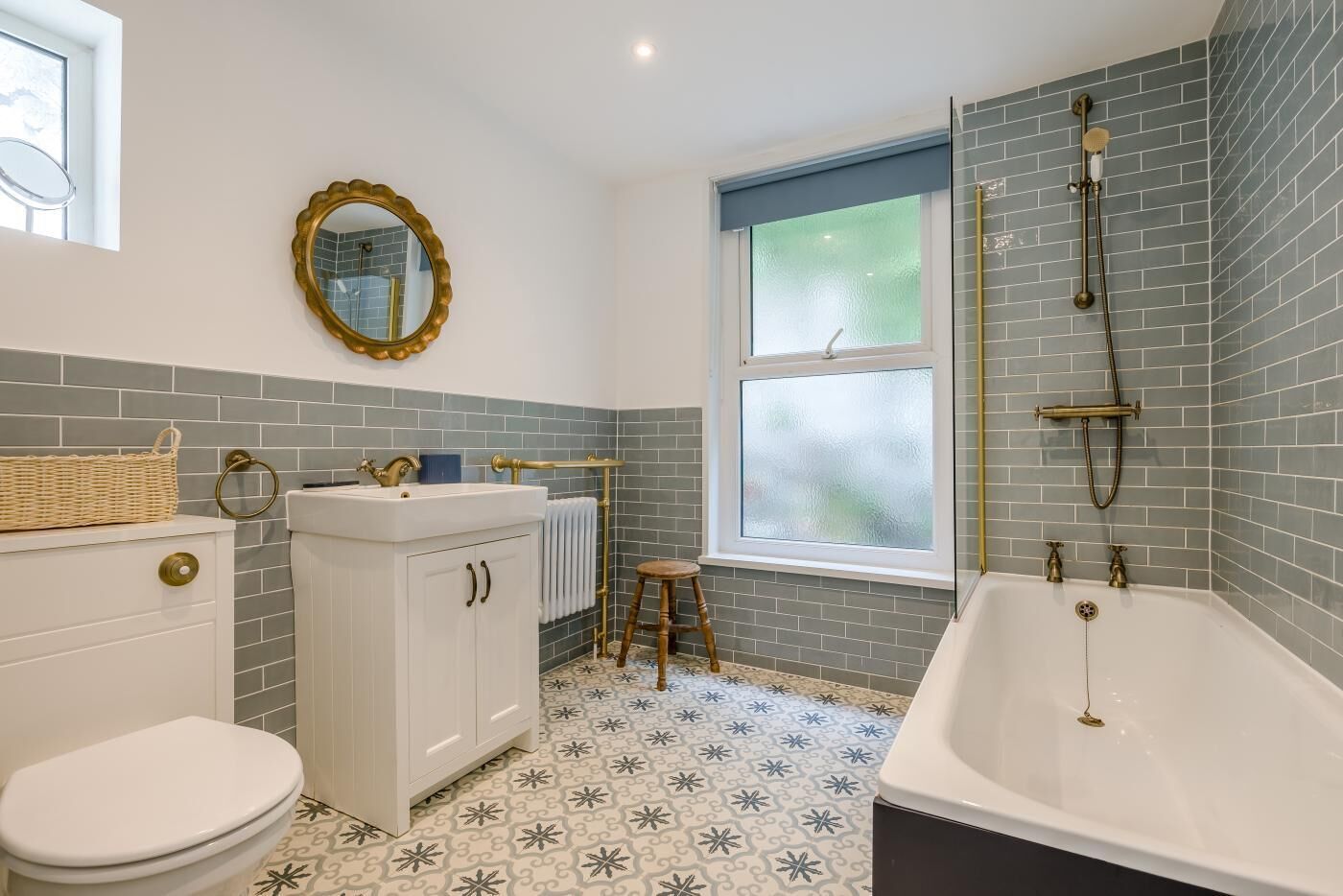 A bathroom with a white toilet, a white sink with gold fixtures, a bathtub with a showerhead, and a window with frosted glass.