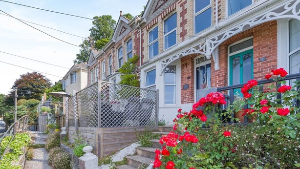 Une rangée de maisons mitoyennes, chacune dotée d’un balcon et d’un jardin agrémenté de fleurs rouges.
