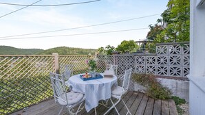 Une terrasse extérieure avec une table ronde et des chaises, une clôture blanche et une vue sur des collines verdoyantes.